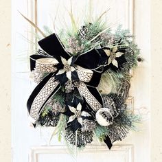 a black and white christmas wreath hanging on a door with pine cones, evergreens and bells