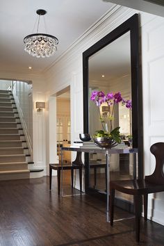 a mirror sitting on the side of a wall next to a table with flowers in it