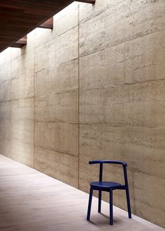 a blue chair sitting in front of a stone wall next to a wooden floor and ceiling