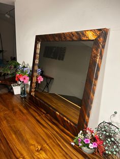 a mirror sitting on top of a wooden floor next to a vase filled with flowers