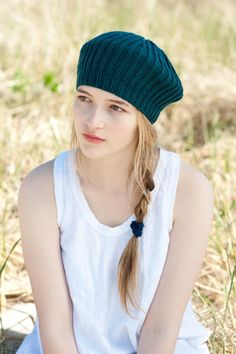 a young woman sitting in the grass wearing a green knitted hat with braids