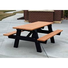 a wooden picnic table sitting on top of a cement floor next to a brick building