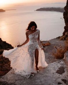 a woman in a white dress is walking up some steps near the water at sunset