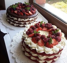 two cakes with strawberries and chocolate frosting sit on a table near a window