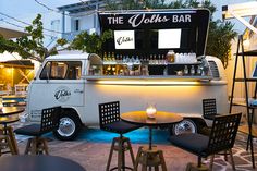 an old vw bus converted into a bar with lights on the side and chairs around it