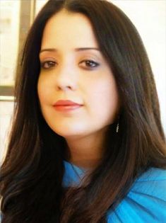 a woman with long dark hair wearing a blue shirt and earrings looking at the camera