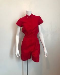 "1960's Broderick 'Official Gym Wear' 100% sanforized red cotton romper.  Cool (as in color) red romper with 1 3/4\" button down collar, 7 metal snaps down front, 1 1/2\" waistband at front, 7 1/4\" pocket at each hip and elasticized waistband at back. Fitted bodice and back yoke with pleats.  Very good condition. Size 32.  sleeve 4 1/2\" shoulder 5 1/4\" shoulder to shoulder 14\" chest 32\" waist 27\" hips 35\" rise front 12 1/2'         back 13 1/2\" inseam 5\" hem 9 1/4\" laid flat, 18 1/2\" total shoulder to waist 17 1/2\" length 35 1/2\"" Vintage Jumpsuits And Rompers For Summer Workwear, Vintage Summer Jumpsuits And Rompers For Work, Retro Summer Workwear Jumpsuits And Rompers, Retro Summer Jumpsuits And Rompers For Work, Retro Cotton Fitted Jumpsuits And Rompers, Vintage Cotton Jumpsuits And Rompers With Short Sleeves, Collared Cotton Jumpsuit With Buttons, Cotton Collared Jumpsuit With Buttons, Red Retro Jumpsuits And Rompers For Summer