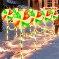 several candy canes are lined up in the snow near a house with christmas lights on it