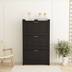 a black cabinet with three drawers next to a chair and potted plant on the floor