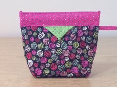 a pink and black purse with polka dots on the front, green triangle in the middle