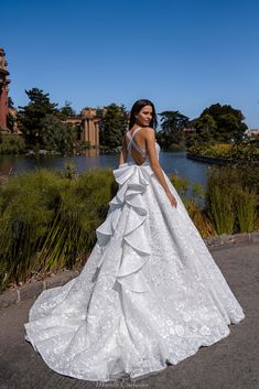 a woman in a white wedding dress standing on the side of a road next to a lake