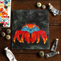 a painting of a crab on a wooden table next to seashells and paintbrushes