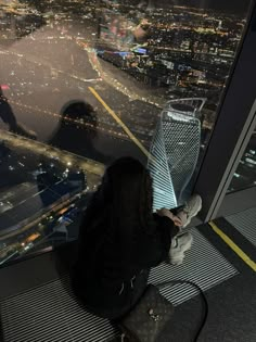 a woman sitting on top of a tall building looking out at the city from an observation platform