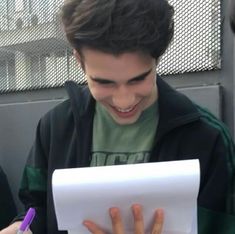 a young man smiles as he looks at his paper while holding a pen and writing on it