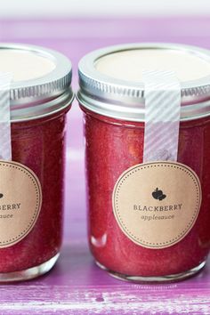 two jars filled with red liquid sitting on top of a purple tableclothed surface