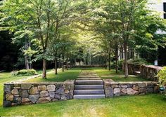 a stone wall with steps leading up to it in the middle of a grassy area