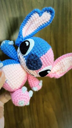 a crocheted blue and pink stuffed animal is held up by someone's hand