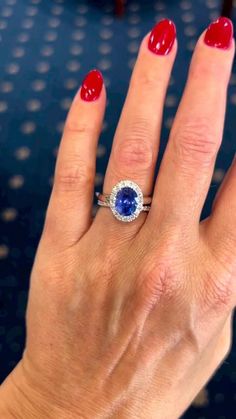 a woman's hand with red and white nail polish holding a blue diamond ring