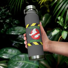 a person holding a black insulated water bottle in front of green plants and leaves