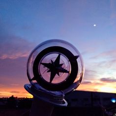 a glass ball with a star in it sitting on top of a metal pole at sunset