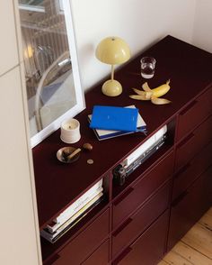 a wooden dresser topped with books and a blue binder next to a lamp on top of it