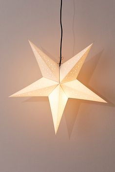 a white paper star hanging from a black string on a gray wall with the light turned on