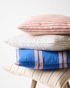 four pillows stacked on top of each other in different colors and sizes, all sitting on a stool