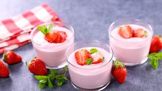 three small glasses filled with yogurt and strawberries on top of a table