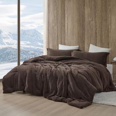 a bedroom with a large bed covered in brown blankets and pillows, along with a mountain view