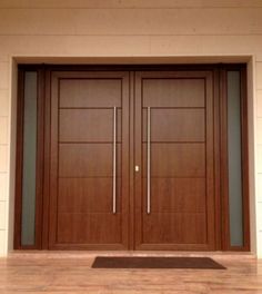 two wooden doors with metal handles in front of a white wall and wood flooring