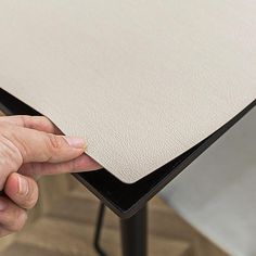 a hand is holding the edge of a table with a white cloth covering it and black legs