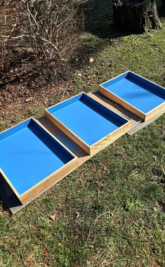 three blue trays sitting on top of the grass in front of a wooden bench