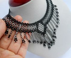 a hand holding a black and silver beaded necklace on a mannequin head