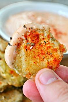 a hand holding up a small cracker with dipping sauce in the bowl behind it