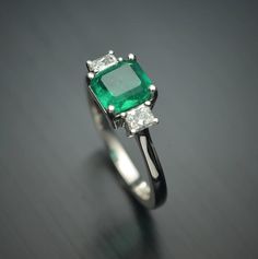 an emerald and diamond ring on a black surface