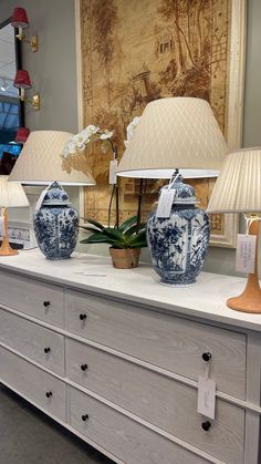 two blue and white vases sitting on top of a dresser next to lamp shades