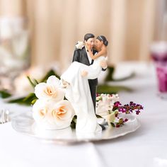 a bride and groom figurine sitting on top of a cake plate with flowers