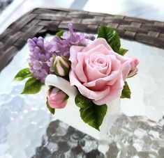 a pink rose sitting on top of a white vase filled with purple and green flowers