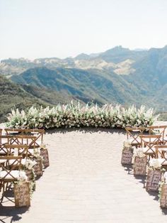 an outdoor ceremony set up with wooden chairs and floral arrangements on the aisle, overlooking mountains