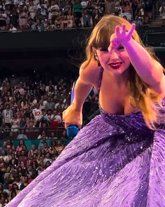 a woman in a purple dress standing on top of a stage with her hands up