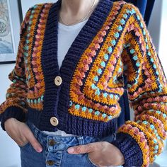 a woman wearing a colorful crocheted cardigan and denim jeans with her hands in her pockets