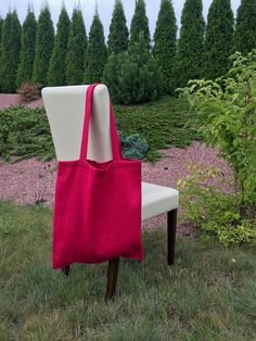 a red tote bag sitting on top of a white chair in the grass next to trees