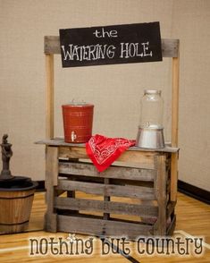 a sign that says the watering hole on top of a wooden crate with two buckets