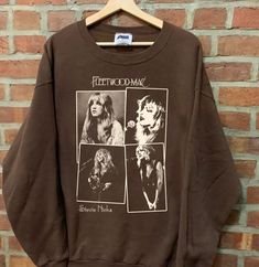 a brown sweatshirt with photos of women from the fleetwood era on it, hanging against a brick wall