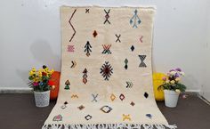 a white rug with colorful designs on it next to some flowers and potted plants