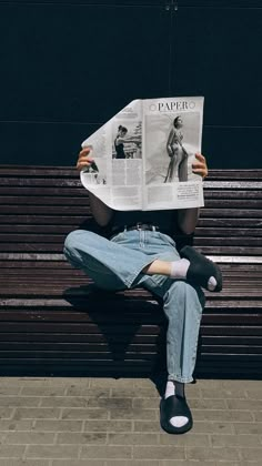 a person sitting on a bench reading a paper with their feet up in the air