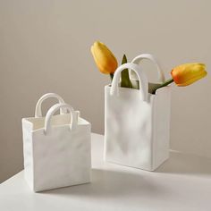 two white bags with yellow tulips in them are sitting on a countertop