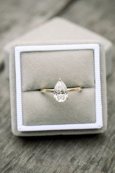 an engagement ring with a pear shaped diamond sits in a velvet box on a wooden table