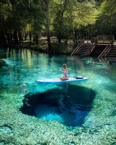 a woman is sitting on a surfboard in the middle of a river with blue water