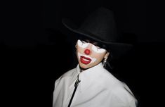 a woman with white makeup and red nose wearing a black hat